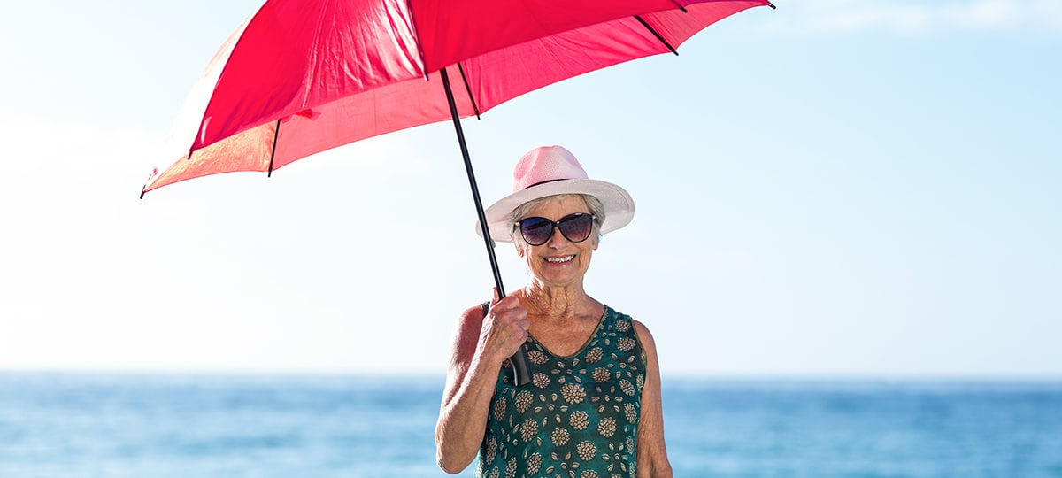 Woman with Hat and Sunglasses Using Umbrella to Shade Her from the Sun